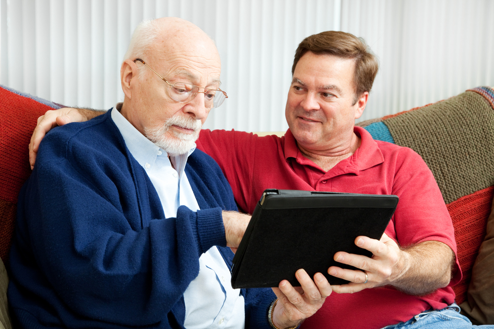 adult son teaching his father to use a new tablet PC